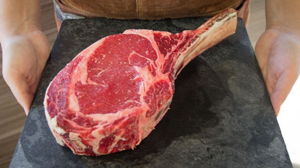 Sepotong daging sapi tomahawak mentah sebagai bahan baku tomahawk beef steak.